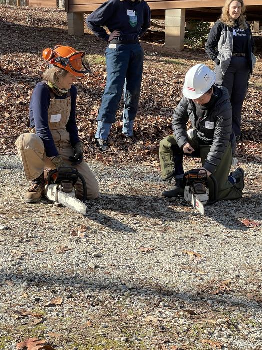 Liz Snider, Woodlands Restoration LLC, instructing participant on how to start a saw. 