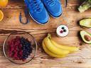 Blue running shoes and assorted healthy foods—bananas, berries, avocado, yogurt on wooden table