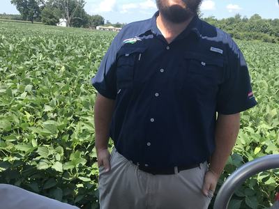 Bearded man wearing cap and sunglasses standing in front of a soybean field