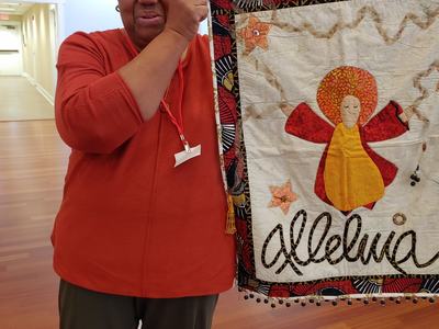 Woman holding quilt with angel applique and text "Alleluia"