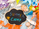 Chalkboard reading "SUMMER CAMP" surrounded by seashells, colorful ribbons, and a pinwheel