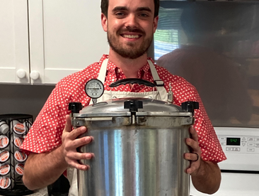 Man holding large stainless pressure canner in kitchen; sticker reads NC Cooperative Ext.