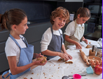 Three children in aprons rolling dough and cutting cookies on a flour-dusted countertop