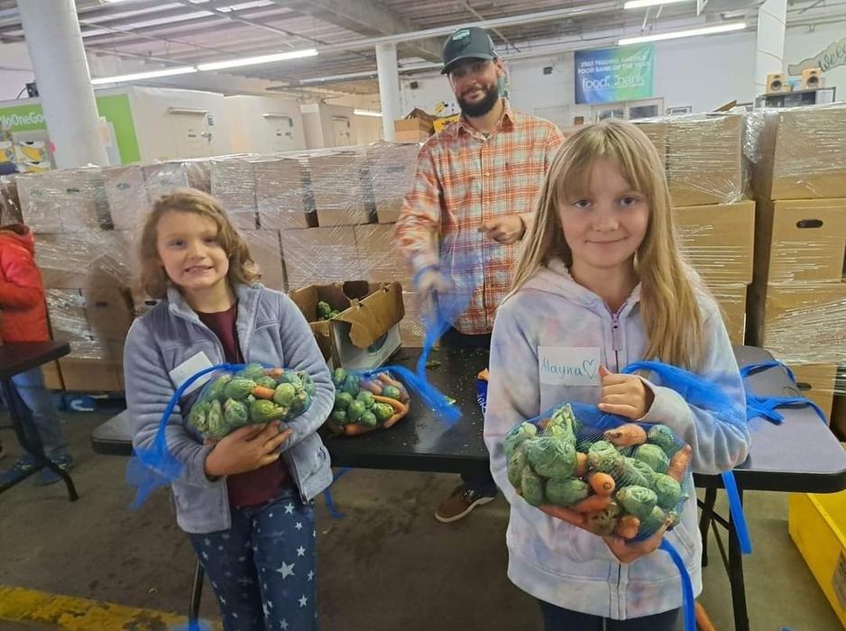 Two girls hold bags of produce at a warehouse.
