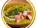 Bowl of pea soup topped with diced ham, thyme sprigs, cream swirl and olive oil