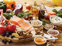 Assorted healthy foods on wooden board: salmon, tomatoes, vegetables, nuts, grains, oils