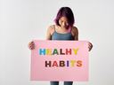 Person holding pink poster that reads "HEALTHY HABITS"