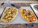 Two oblong homemade pizzas with mozzarella, yellow peppers, red onion on cutting board