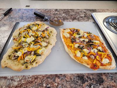 Two oblong homemade pizzas with mozzarella, yellow peppers, red onion on cutting board