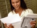 Woman at bank of mailboxes holding and reading letters and a flyer.