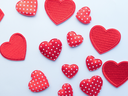 Scattered red fabric hearts, some solid and some white polka-dotted, on a white background