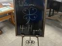 Chalkboard on easel reading "Welcome" and "4‑H guests" with a drawn four-leaf clover