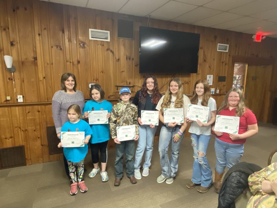 Adult and seven children holding "CERTIFICATE" papers in a wood-paneled room