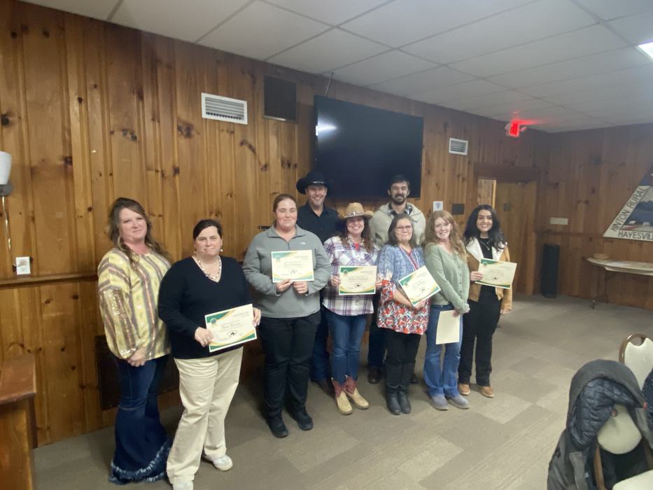 Nine people standing in a wood-paneled room holding certificates for recognition