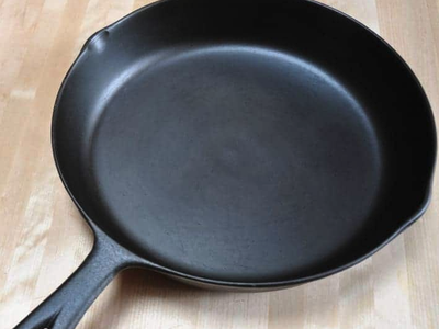 Cast-iron skillet on wooden surface, empty, showing handle and two pour spouts