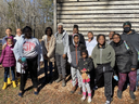 Group of people of various ages standing outdoors in front of a weathered wooden building