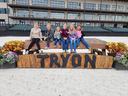 Six children sitting on a wooden beam above a sign reading "TRYON" at an outdoor arena