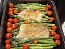 Two baked fish fillets on asparagus with cherry tomatoes in a roasting pan