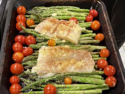 Two baked fish fillets on asparagus with cherry tomatoes in a roasting pan