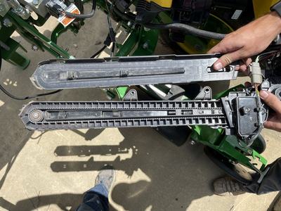 Hands holding opened plastic belt/gear housing with visible spring and wiring on green farm implement