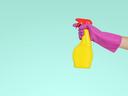 Hand in pink glove holding yellow spray bottle with red nozzle on teal background