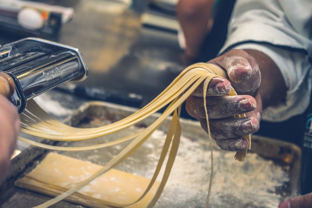 Floured hand guiding freshly cut pasta noodles from a pasta machine