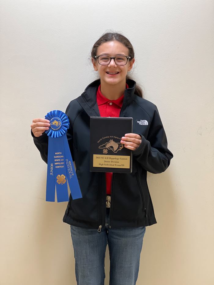Young person holding blue ribbon and plaque reading "2023 NC 4‑H Hippology Contest Junior Division"
