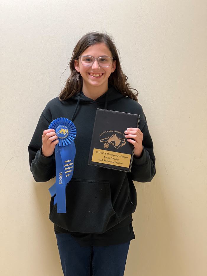 Person holding blue ribbon labeled "Junior" and plaque reading "2023 NC 4‑H Hippology Contest Junior Division"