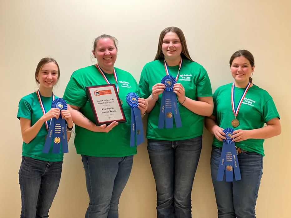 Four individuals in green shirts holding blue ribbons and plaque reading "Champion Junior Team"