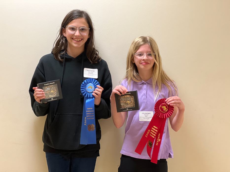 Two girls holding plaques and blue and red ribbons reading "North Carolina"