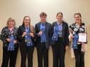 Five people standing holding blue ribbons and a plaque reading "Champion Senior Team"