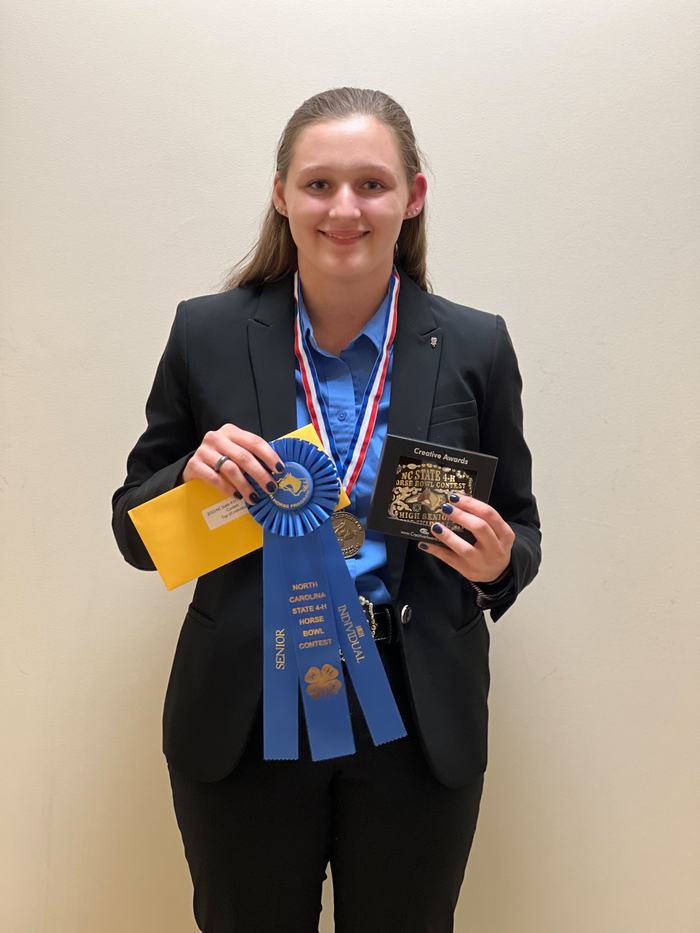 Blazer-clad person holding blue ribbon "NC State 4‑H Horse Bowl Contest", medal, plaque, envelope