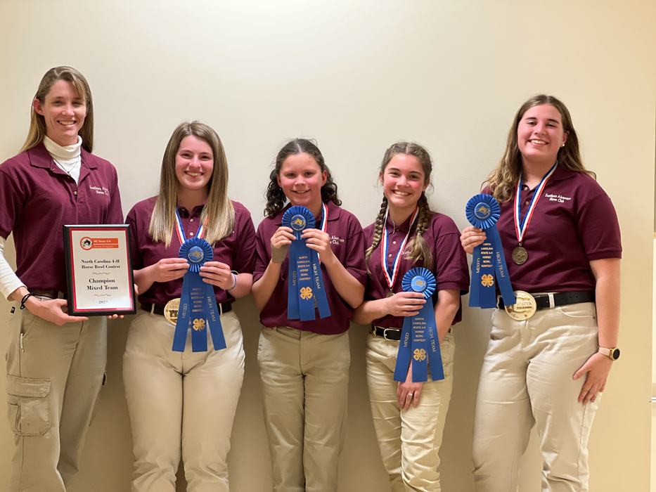 Five 4-H members in maroon shirts holding blue ribbons and a plaque reading "Champion Mixed Team"