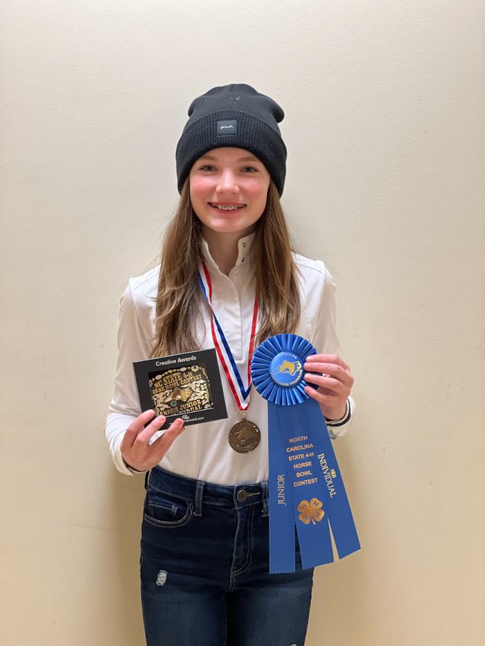 Youth in black beanie holding blue ribbon "NC State 4‑H Horse Bowl Contest", medal and plaque