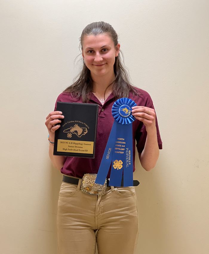 Person holding blue ribbon reading "North Carolina State 4-H Hippology Contest" and a plaque