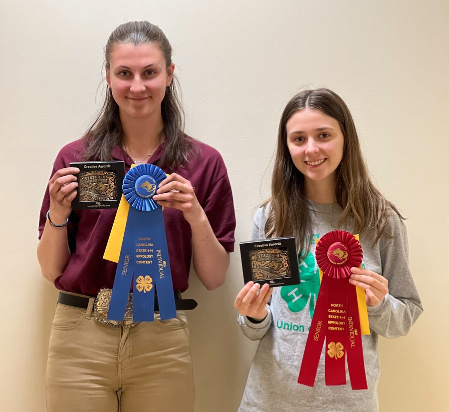 Two people holding awards and blue and red ribbons reading "North Carolina State 4‑H Hippology Contest."