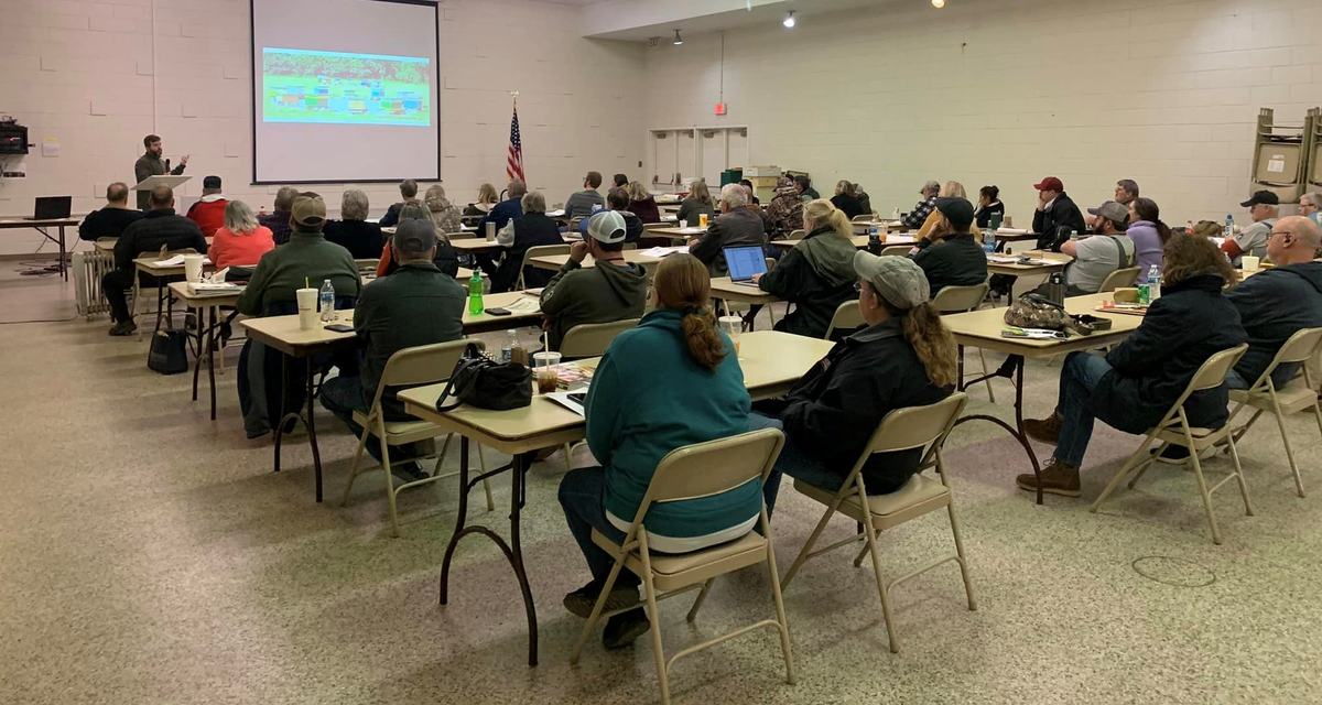 A group sits at tables listening to a presentation.