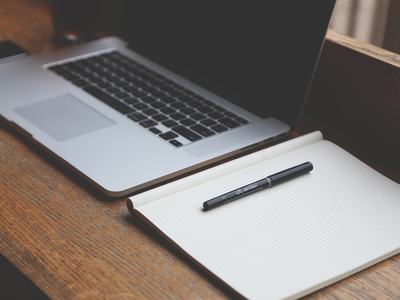 Desk with open laptop, open notebook and black pen