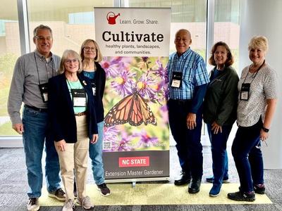 A group of Master Gardener volunteers pose for a picture beside a colorful banner.