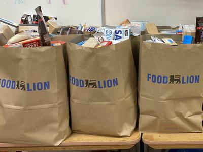 Three brown Food Lion grocery bags filled with assorted food items on tables