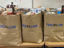 Three brown Food Lion grocery bags filled with assorted food items on tables