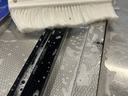White scrub brush resting on wet metal tracks and textured surface with soap suds