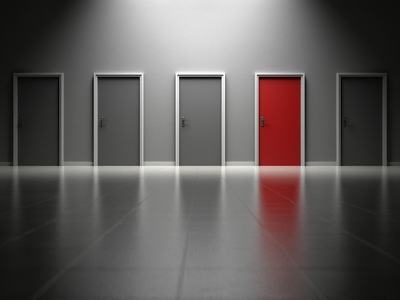 Seven closed doors in a dim hallway, one door red and spotlighted