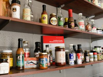 Shelves with condiment bottles and a red booklet labeled "Acidified Foods Manufacturing School"