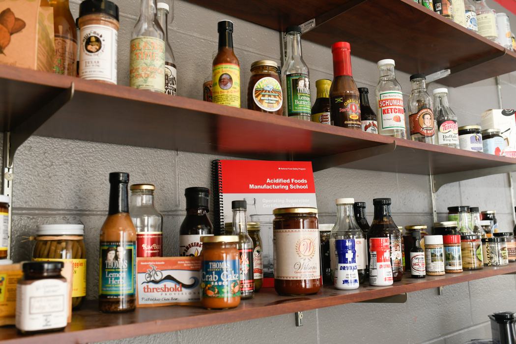 Shelves with condiment bottles and a red booklet labeled "Acidified Foods Manufacturing School"