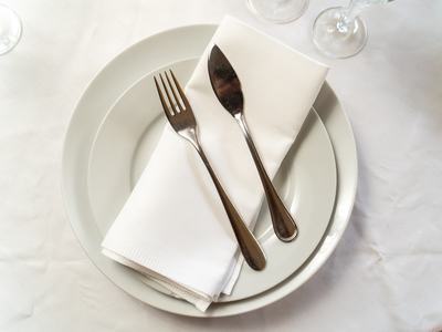 White dinner plate with folded napkin and a fork and knife placed on top