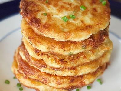 Stack of golden potato pancakes topped with chopped chives on a plate