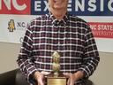 Man holding peanut-shaped trophy reading "2022 Chowan County Champion Peanut Producer"