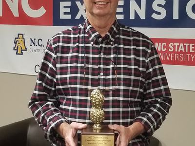 Man holding peanut-shaped trophy reading "2022 Chowan County Champion Peanut Producer"