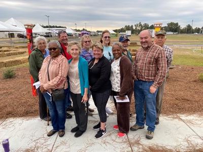 Twelve adults standing together outdoors near event tents and hay bales.